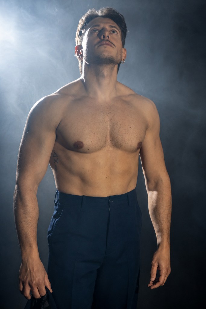 Shirtless man standing in smoke and backlight, looking upward.